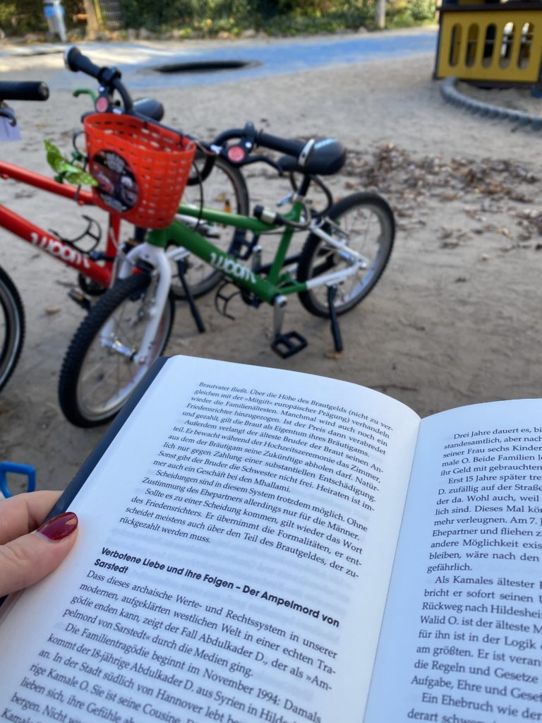 Auf dem Spielplatz ein Buch lesen und den Kindern beim Spielen zuschauen
